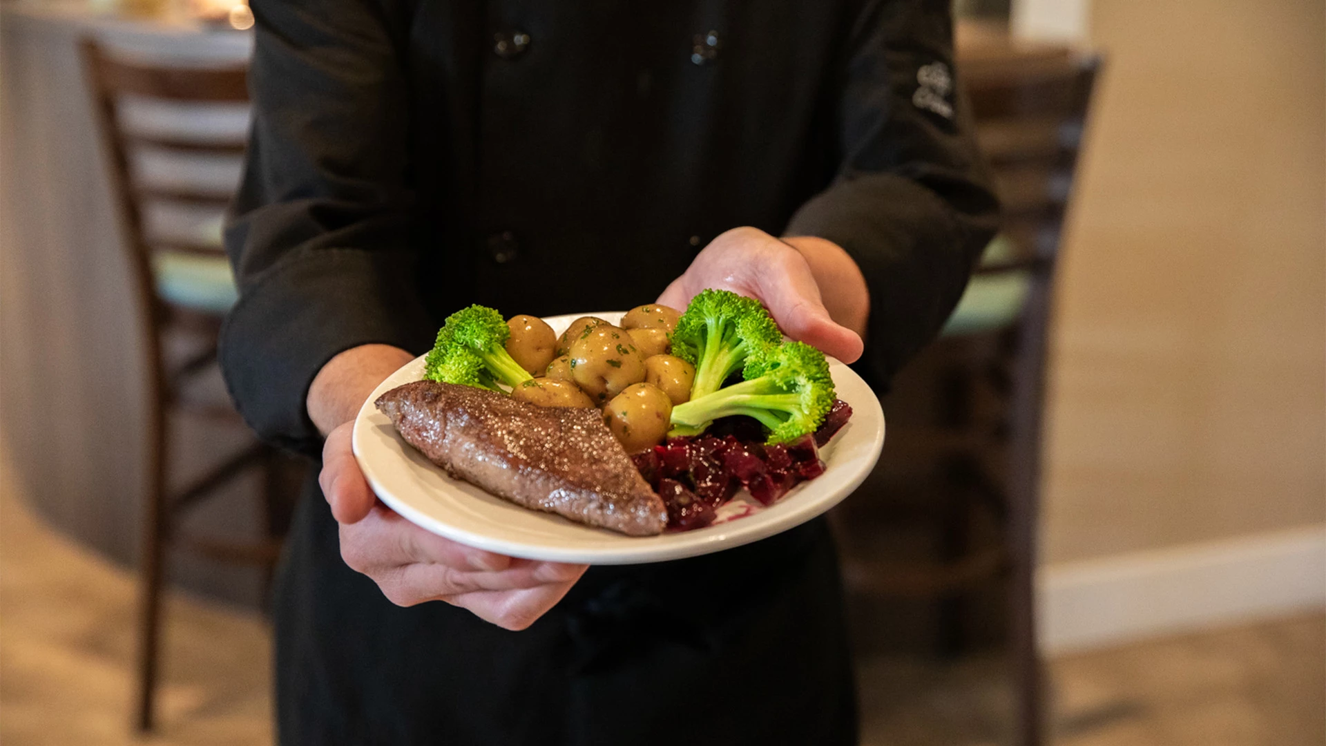 Chef holding a plate of steak, broccoli and potatoes